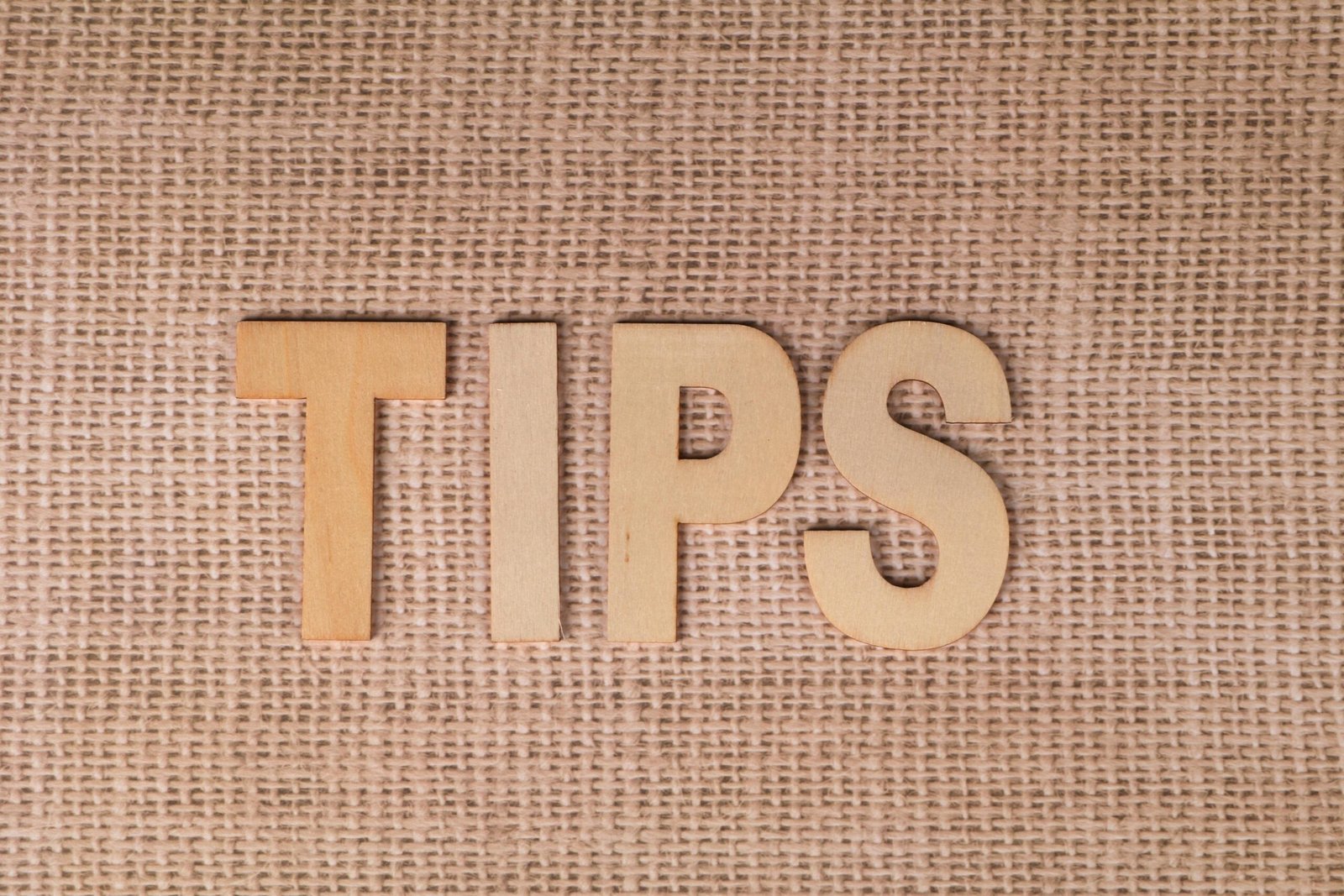 The word 'TIPS' in wooden letters on a burlap background, ideal for business advice visuals.