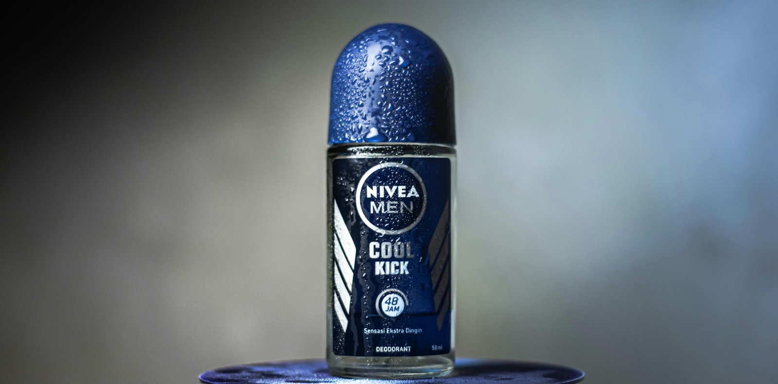 Close-up of Nivea Men Cool Kick deodorant with water droplets on a blurred background.
